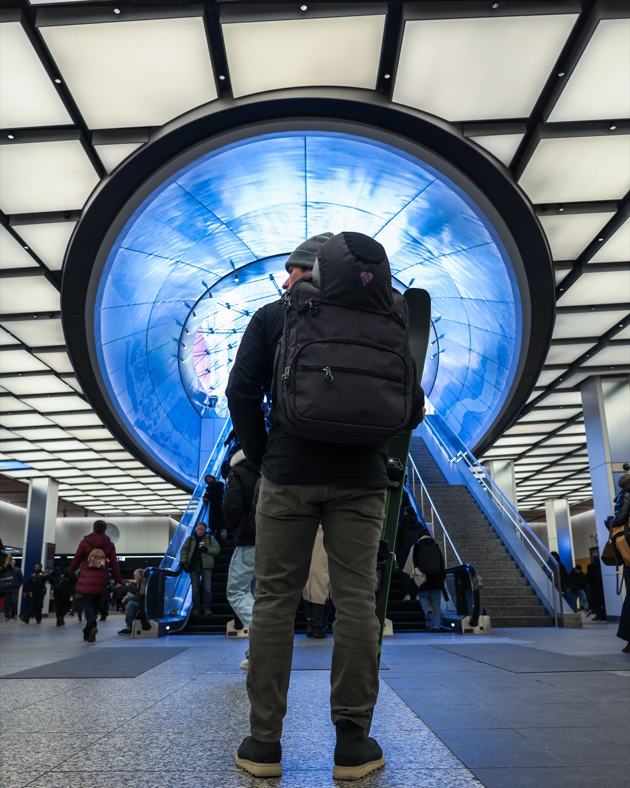Traveler with backpack and skis beneath a domed transit hub skylight